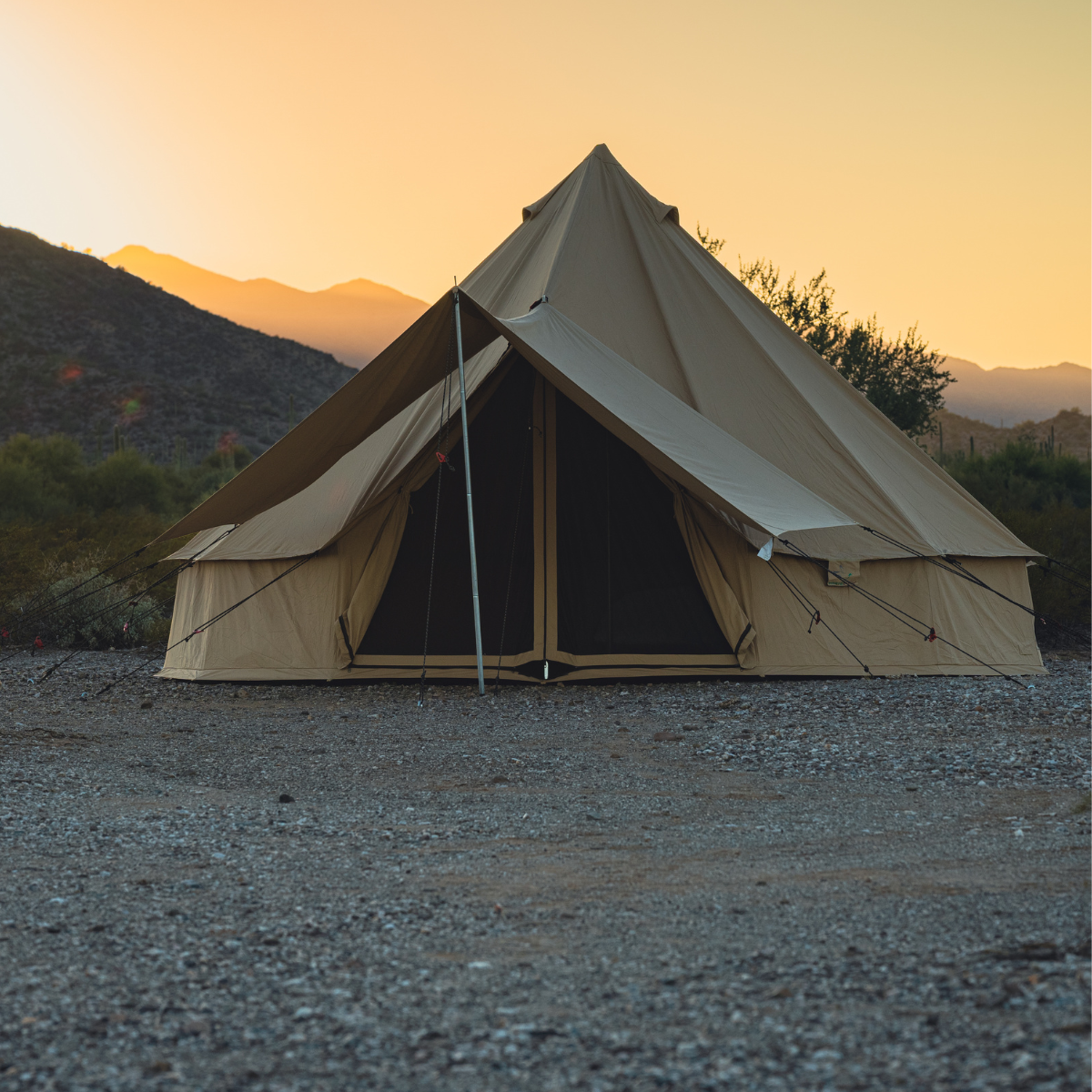 Beige tent in a desert landscape with mountains at sunset