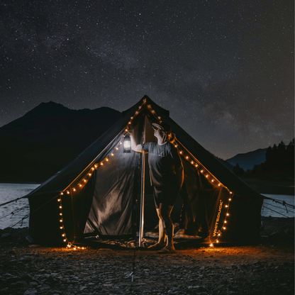 Person standing in front of a tent with string lights under a starry night sky.
