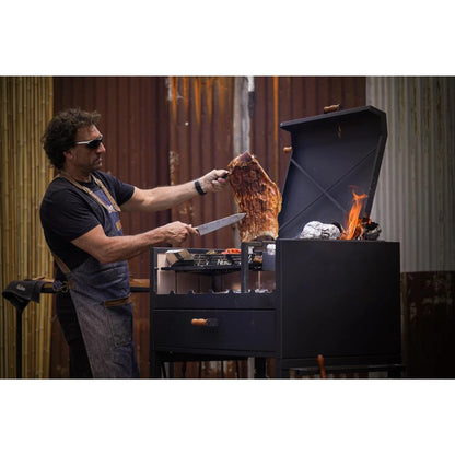 Man grilling meat over a fire pit with flames visible